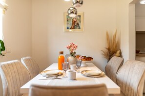 Ein Esstisch mit Stühlen, eine Vase mit Blumen, eine Flasche Orangensaft und ein Teller mit Essen.