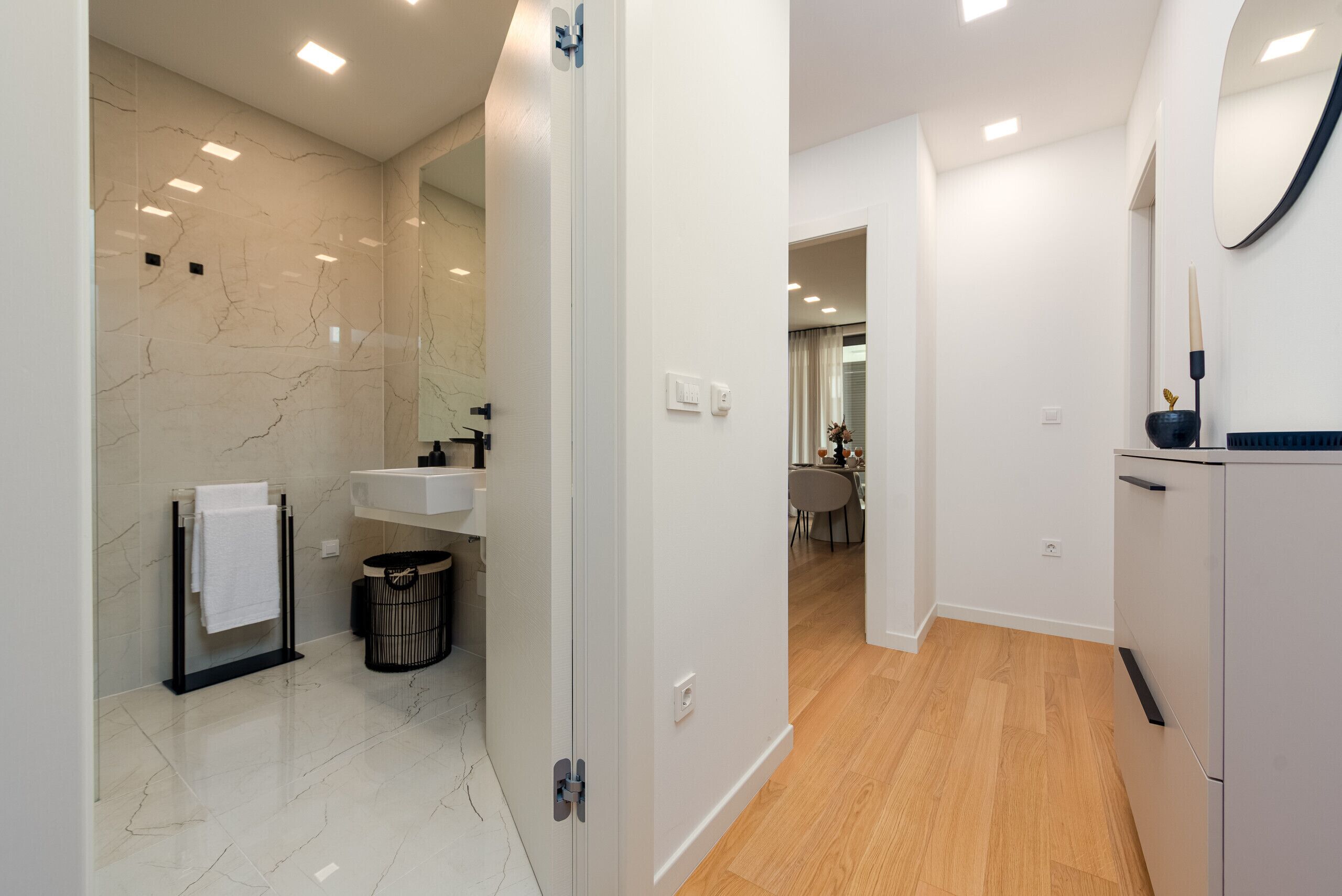Un baño moderno con pared de mármol, un lavamanos, un espejo y un cubo de basura.