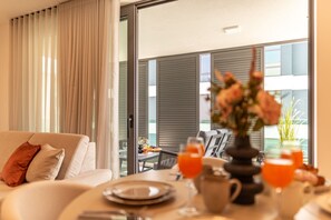 A modern hotel room with a balcony, a dining table set with plates, glasses, and a vase of flowers. - Zaria Luxury Residence (Zadar)