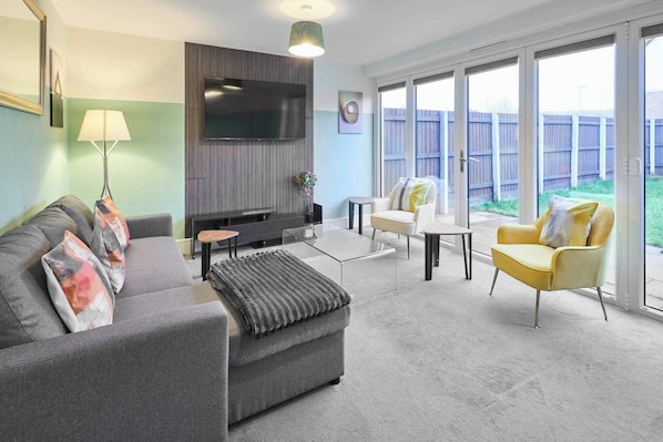 A living room with a sofa, armchair, coffee table, TV, and a balcony with a view.