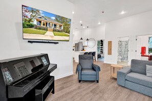Uma sala de estar moderna com uma TV de tela plana, um piano, uma poltrona cinza e um sofá cinza.