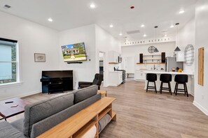 Uma sala de estar moderna com sofá, TV e um espaço de refeições, com cozinha ao fundo.