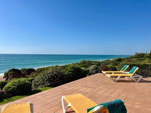 Eine Terrasse mit zwei gelben Liegestühlen, Blick auf den Ozean und einem angelegten Garten.