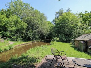 Vista al río con una terraza de madera, una silla y una pequeña mesa.