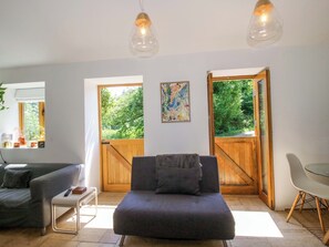 Ein modernes Wohnzimmer mit einer Couch, einem Esstisch und zwei großen Fenstern mit Blick auf Grünflächen.