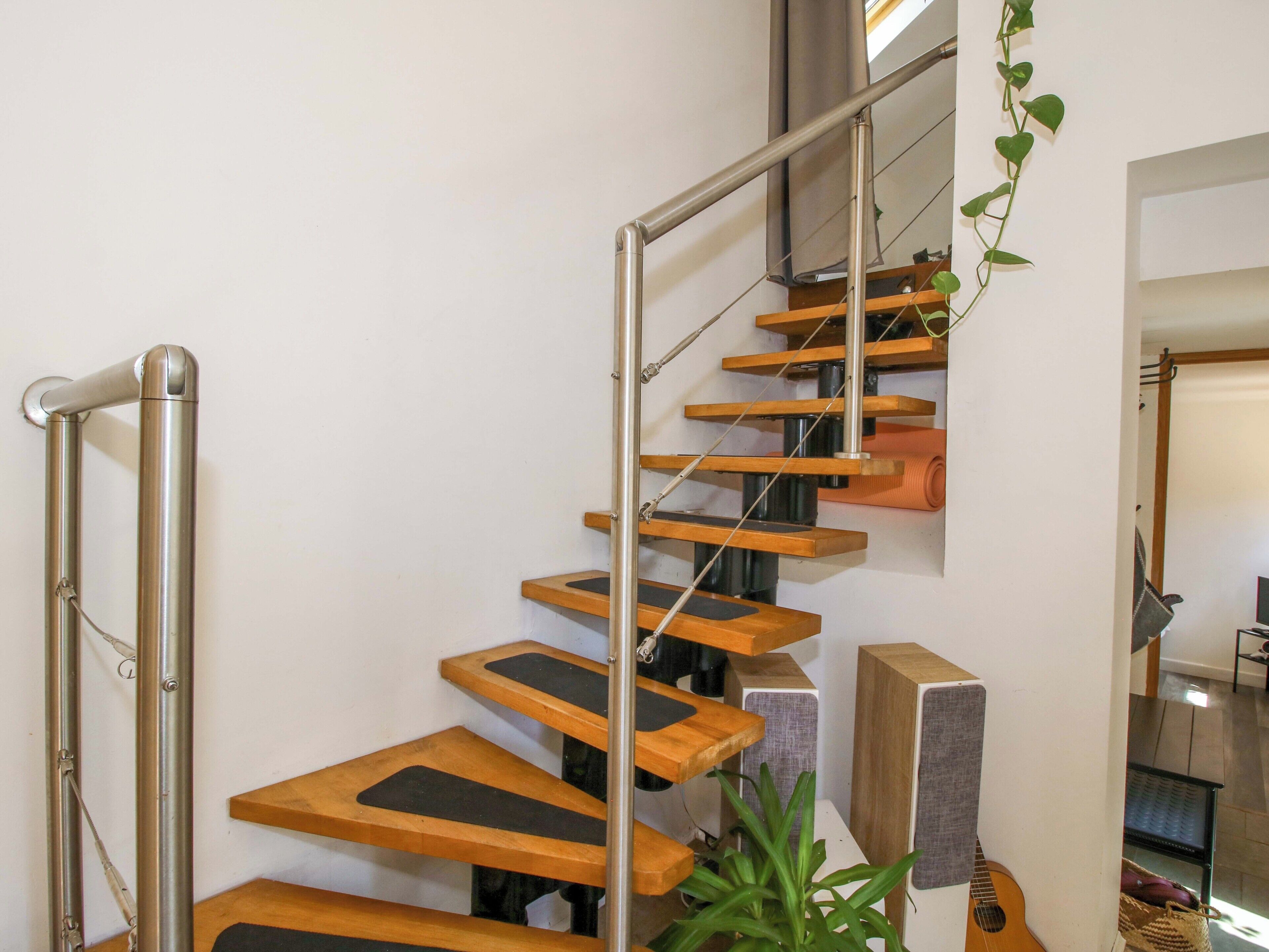 A staircase with wooden steps and metal railings, a plant, and speakers in a room.