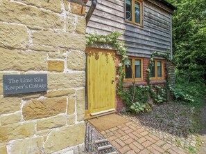 A stone cottage with a wooden door, a sign reading 'The Lime Kiln Keeper's Cottage,' and a brick pathway leading to the entrance. - The Lime Kiln Keepers Cottage (Ellesmere)