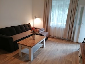 Ein modernes Wohnzimmer mit einer Couch, einem Couchtisch, einer Lampe und Blick durch transparente Vorhänge.