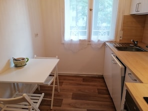 Eine kleine Küchenzeile mit einem weißen Tisch und Stühlen, einem Fenster mit Spitzenvorhängen und einem Holzboden.