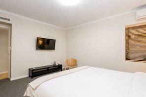 A bedroom with a bed, a TV mounted on the wall, a wooden chair, and a window with blinds. - Luxury West End |heart of Freo | Parking (Fremantle)