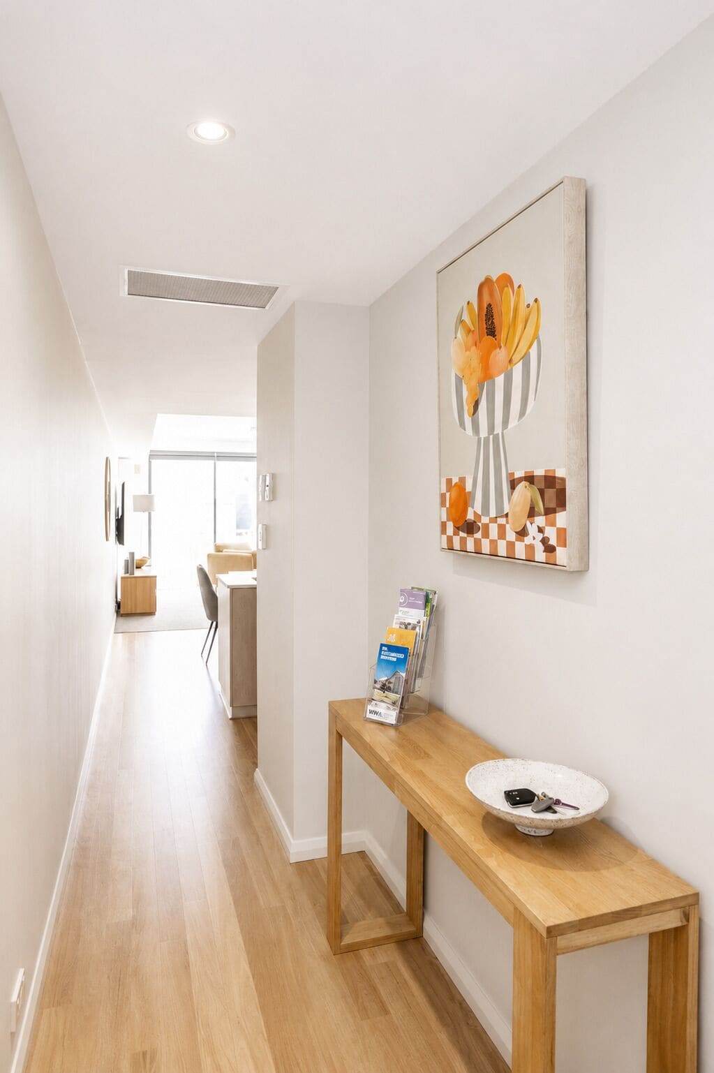 A hallway with a wooden bench, a vase with flowers, and a wall-mounted informational brochure stand.