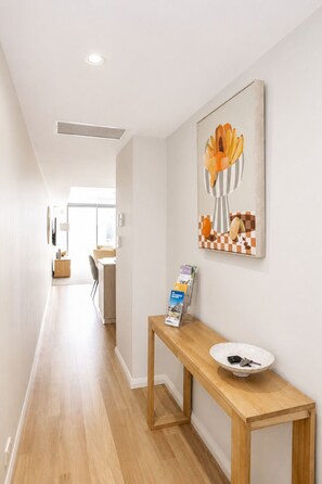 A hallway with a wooden bench, a vase with flowers, and a wall-mounted informational brochure stand. - Luxury West End |heart of Freo | Parking (Fremantle)