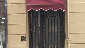 Eine schwarze Tür mit dekorativem Muster, eine rote Markise und ein Schild mit der Aufschrift '1A' an einer beigen Wand.