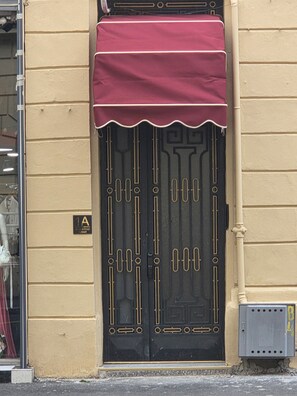 Eine schwarze Tür mit dekorativem Muster, eine rote Markise und ein Schild mit der Aufschrift '1A' an einer beigen Wand.