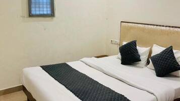 A neatly made bed with white and dark bedding, a small window with a grid pattern, and an air conditioning unit on the wall.