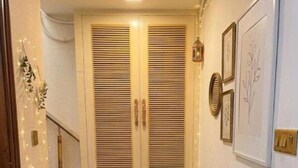 A narrow hallway with a patterned rug, a bench, a small table with a candle, and a large window with shutters. - Hotel Lotus Inn Near By OTABoostup (Chandigarh)