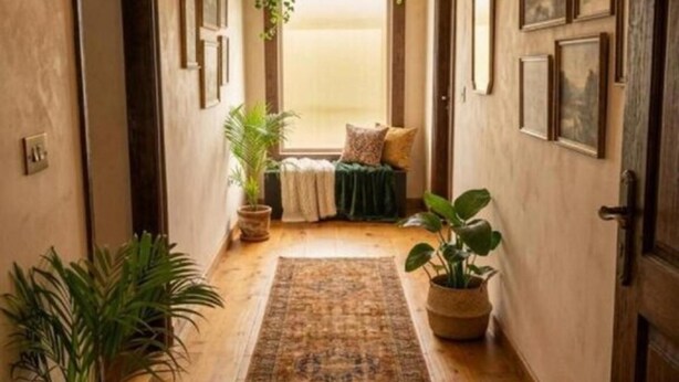A hallway with a wooden floor, a patterned rug, potted plants, framed pictures on the walls, and a ceiling light fixture. - Hotel Lotus Inn Near By OTABoostup (Chandigarh)