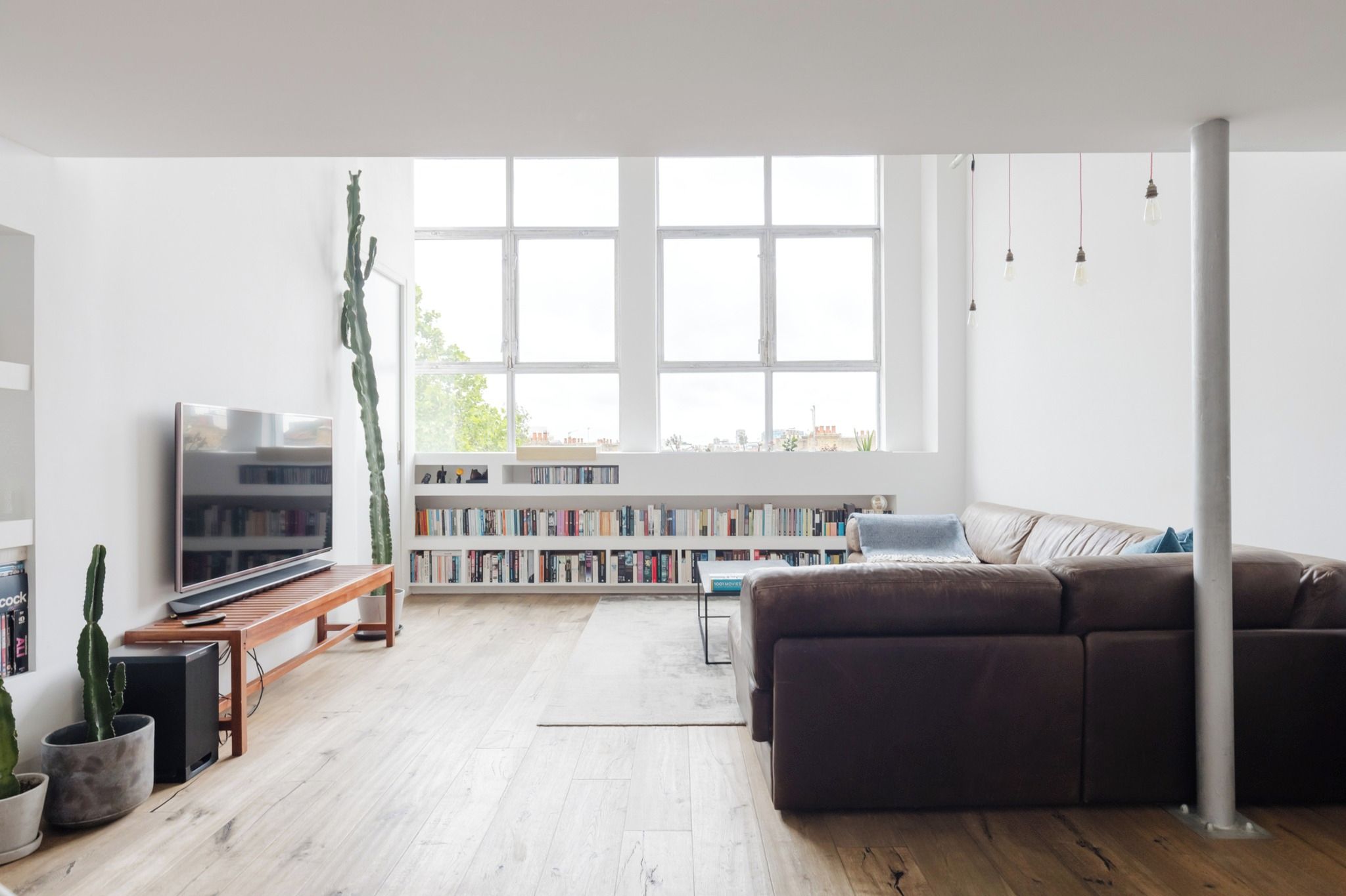 Een moderne woonkamer met een flatscreen televisie, een bruine bank, een houten salontafel, een boekenkast en een groot raam.