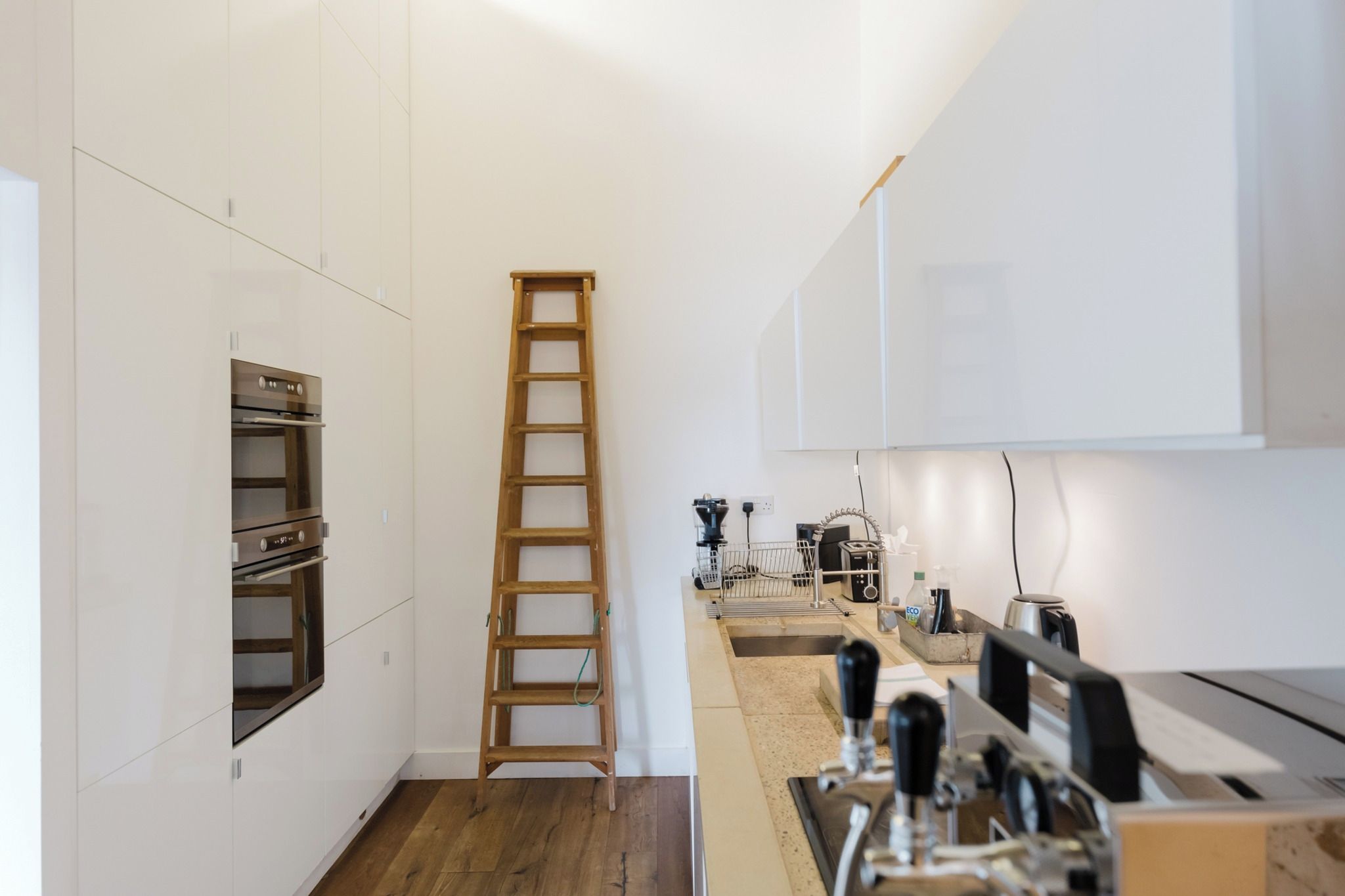 A modern kitchen with white cabinetry, a wooden ladder, and various appliances.