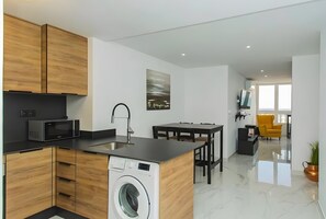 Une cuisine moderne dotée d’un lave-linge encastré, d’un coin repas avec une chaise jaune et d’une grande fenêtre.