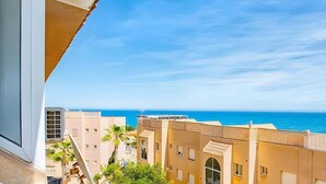 A balcony with a view of the sea, buildings with flat roofs, and a clear sky.