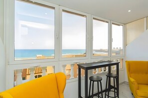 Un balcon avec vue sur la mer, une table avec deux tabourets et deux chaises jaunes.