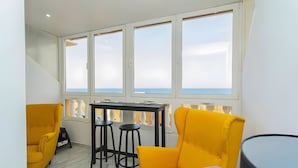 A balcony with a table and two chairs, a view of the sea, and a white railing.