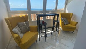 A room with two yellow chairs, a small table, and large windows offering a view of the sea.