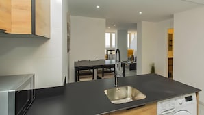 A modern kitchen with a built-in dishwasher, a stainless steel sink, and a dining area with a dark wooden table and chairs.