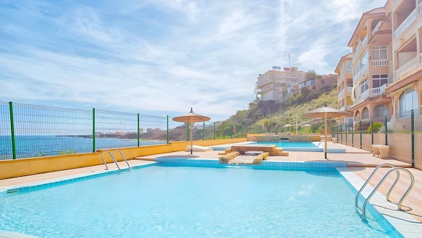 A swimming pool with a view of the sea, a hotel building, and a hillside.