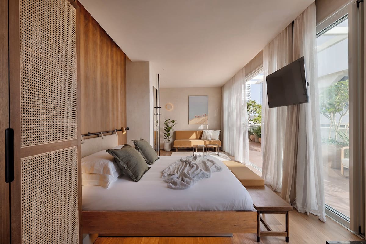 A modern bedroom with a large bed, a sofa, a TV, and a balcony with a view.