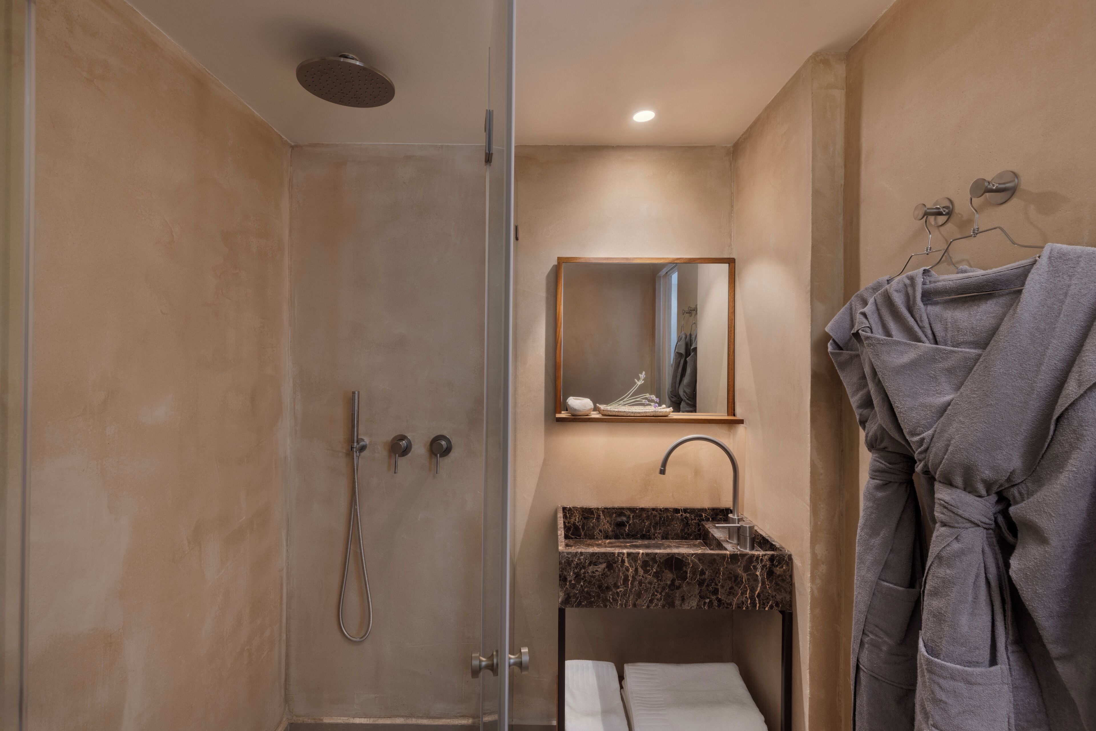Un baño moderno con ducha envuelta en vidrio, lavamanos de mármol, espejo y perchero con bata.