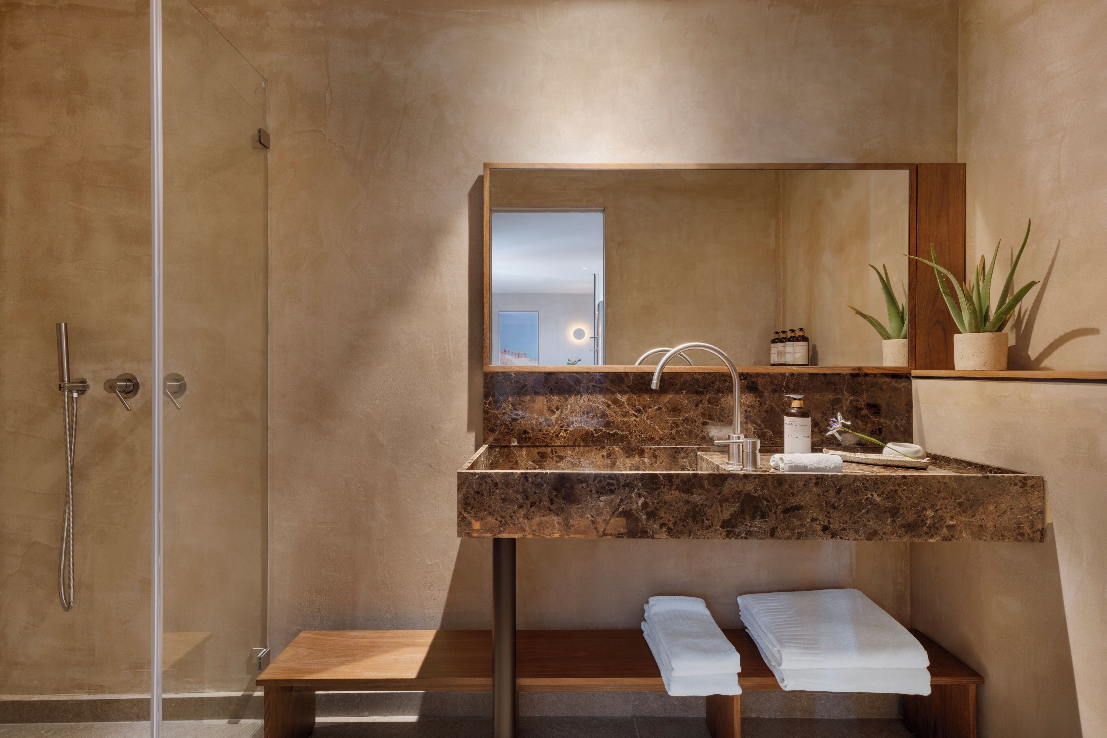 Un baño moderno con cabina de ducha de vidrio, lavamanos de mármol y banco de madera.