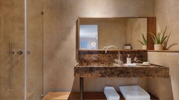 Un baño moderno con cabina de ducha de vidrio, lavamanos de mármol y banco de madera.