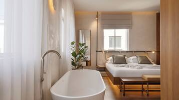 Un dormitorio moderno con una bañera grande, una cama con almohadas, una mesita de noche y un ventanal con vistas.