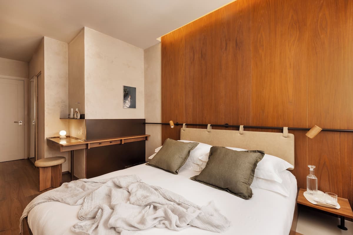 A neatly made bed with pillows, a bedside table with a lamp, and a wooden headboard.