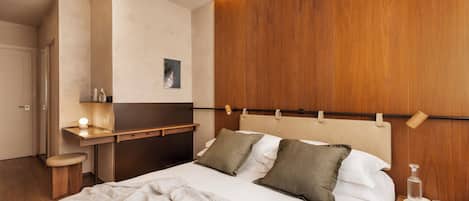 A neatly made bed with pillows, a bedside table with a lamp, and a wooden headboard.
