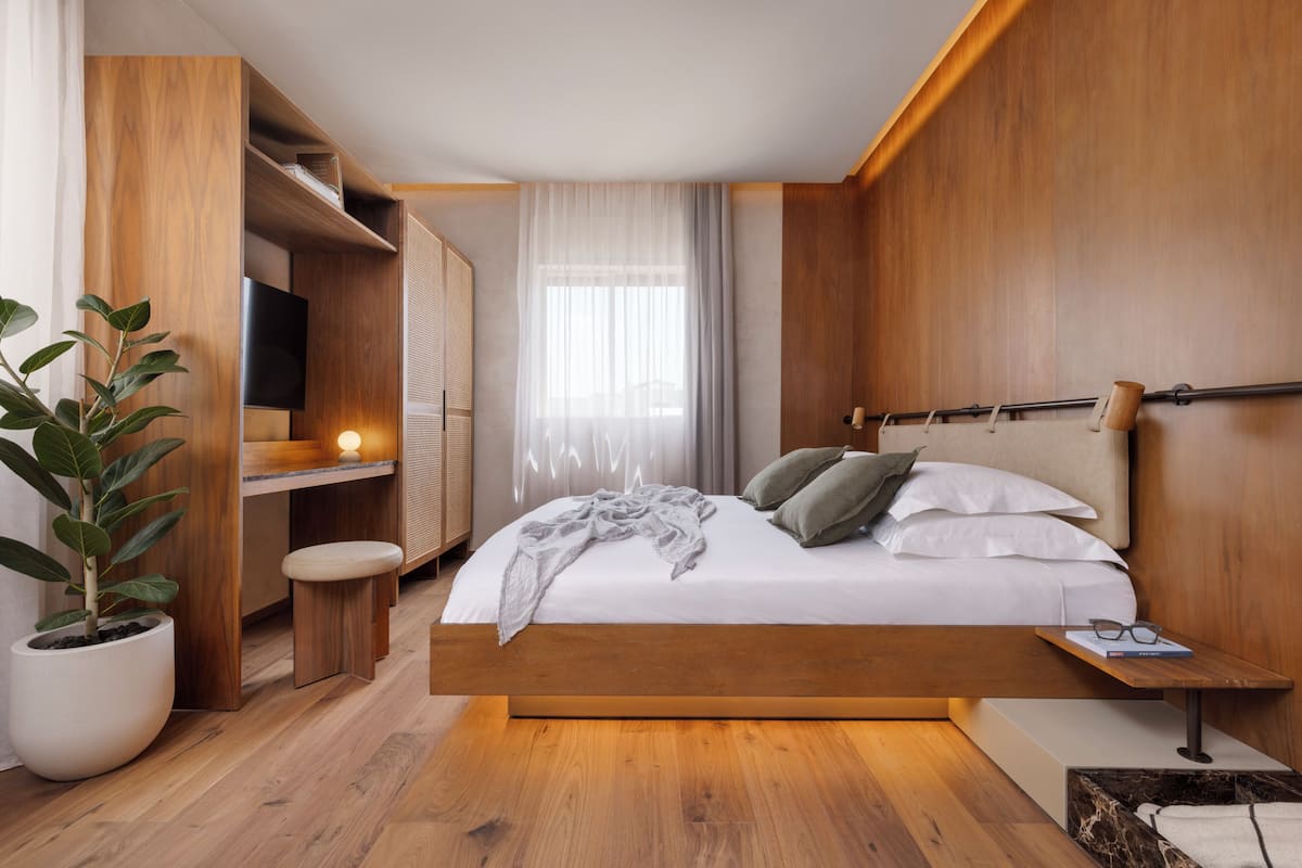 A modern bedroom with a wooden bed, bedside table, and a potted plant.