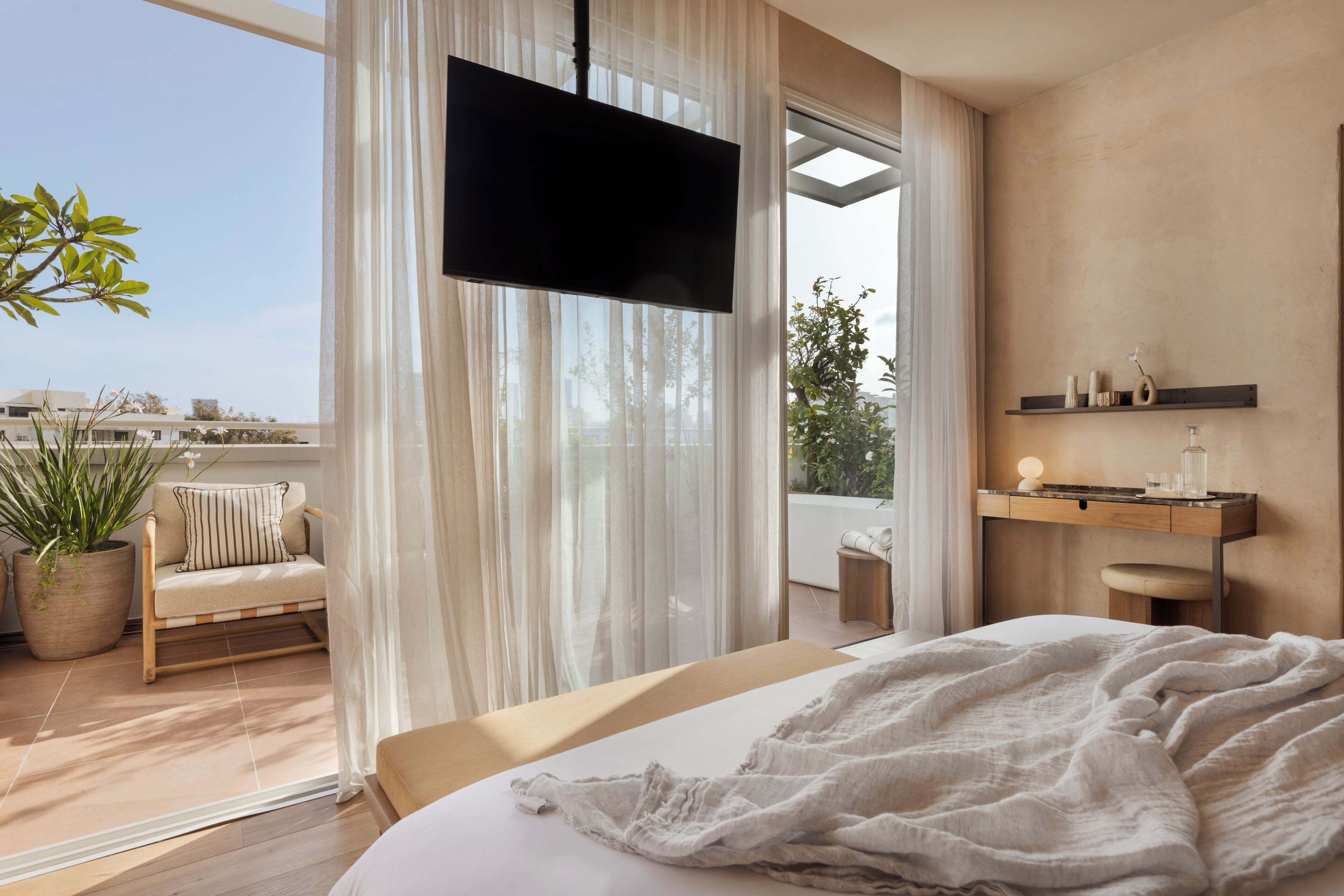 Un dormitorio con cama, televisor, planta en maceta, sofá y balcón con vistas.