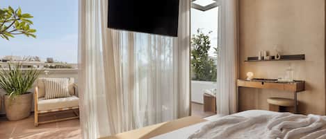 A bedroom with a bed, a TV, a potted plant, a sofa, and a balcony with a view.