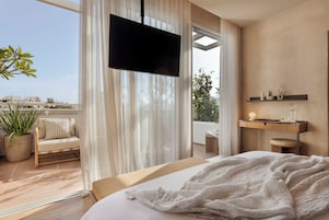 Un dormitorio con cama, televisor, planta en maceta, sofá y balcón con vistas.