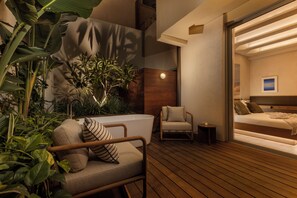 Una habitación moderna con piso de madera, una bañera blanca, una cama con cabecera de madera, una silla y una mesita.