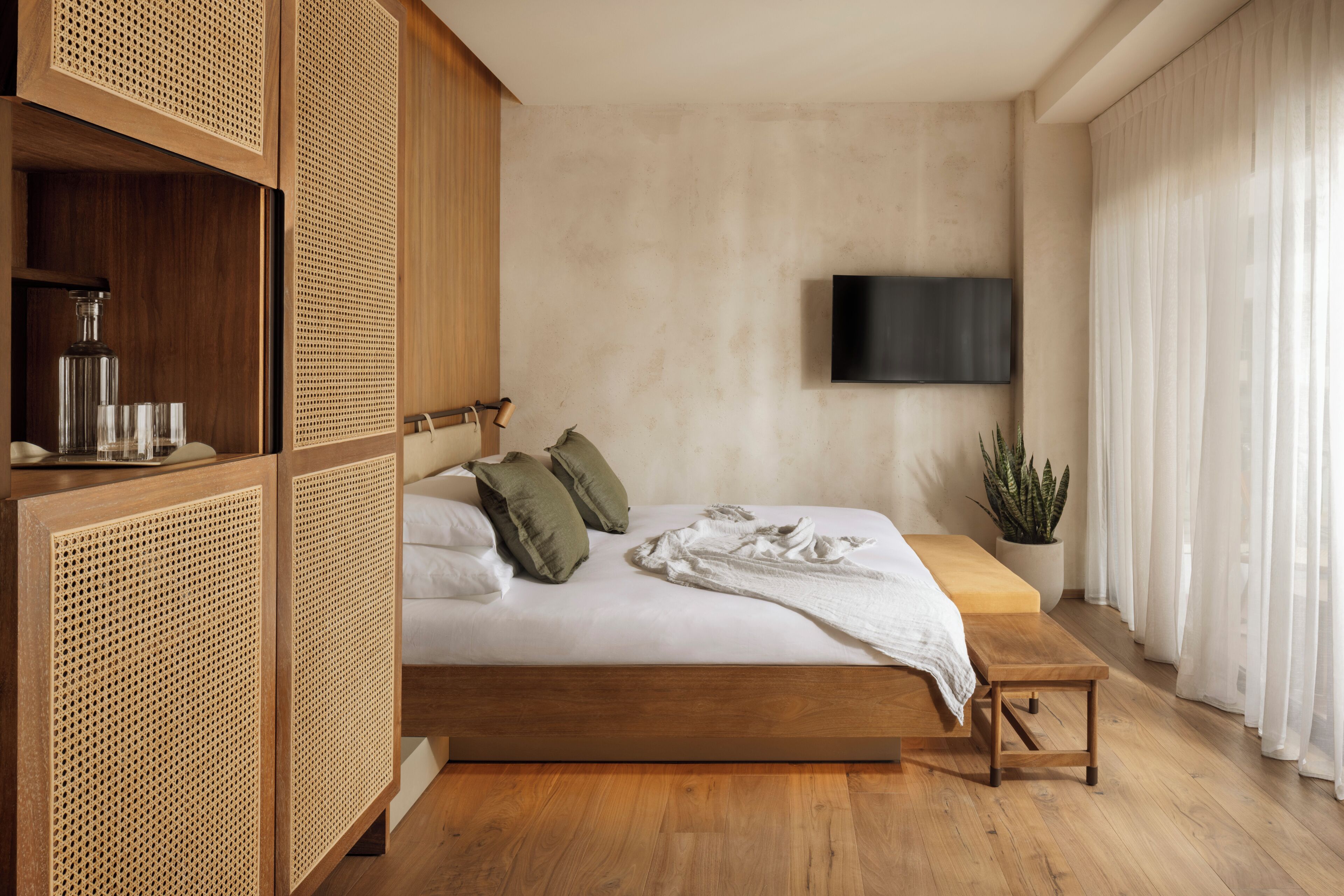 Un dormitorio moderno con una cama de madera, un televisor montado en la pared y una planta en maceta.