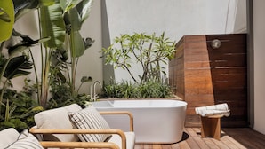 A modern bathroom with a freestanding bathtub, a wooden bench, and lush greenery. - The ABY Hotel  (Tel Aviv)