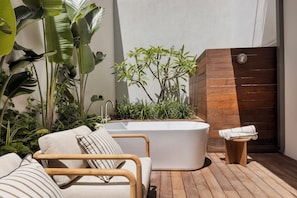 A modern bathroom with a freestanding bathtub, a wooden bench, and lush greenery. - The ABY Hotel  (Tel Aviv)