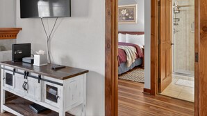 Un dormitorio con cama, televisor montado en la pared, puerta de madera que da a un baño y escritorio con cajones.
