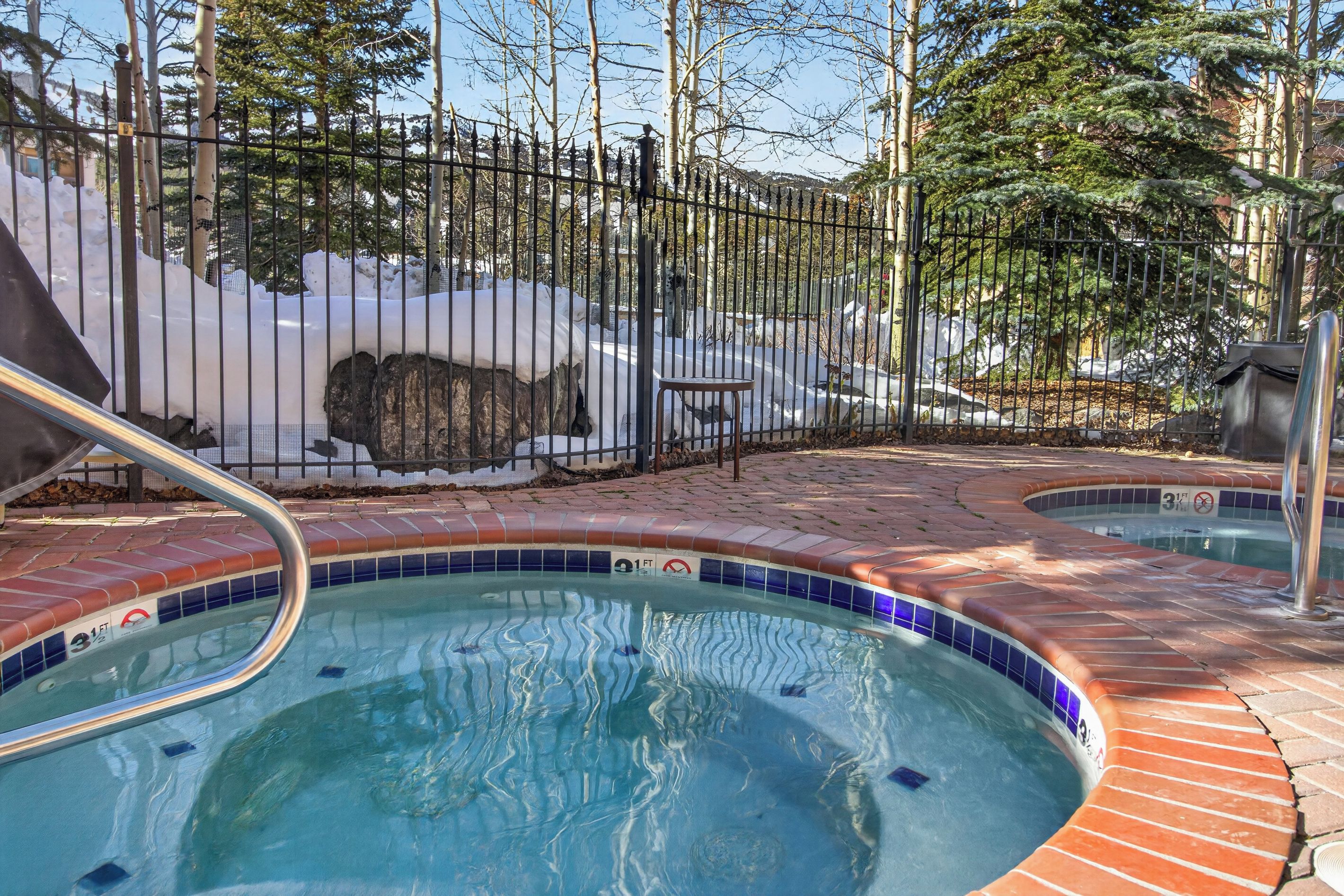 A swimming pool with a tiled edge, a metal fence, and a snow-covered area in the background.
