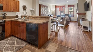 Una cocina con gabinetes de madera, lavavajillas, encimeras de granito y un comedor con mesa y sillas.