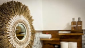Un baño con un espejo redondo, repisa de madera con artículos de aseo y pared con textura.