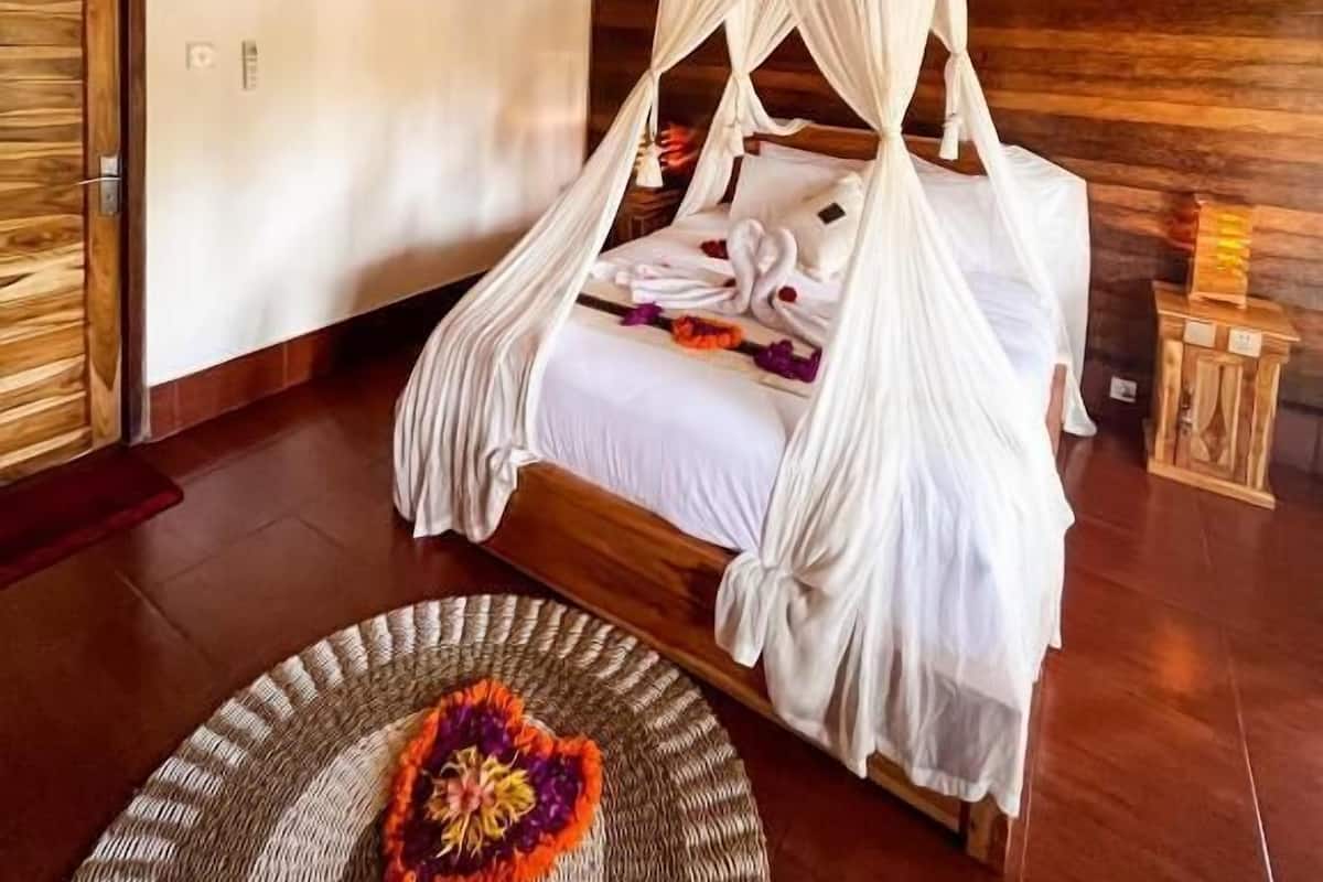 Una cama con dosel y cuatro columnas, cabecera de madera, aire acondicionado de pared y alfombra tejida con diseño de corazón.